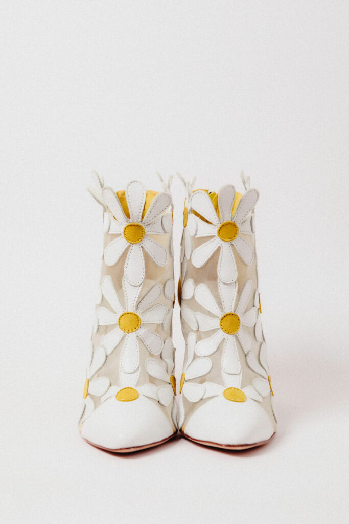 Bota amarela Margarida Boots Giseli Dias com margaridas brancas de couro, transparência e salto bloco.